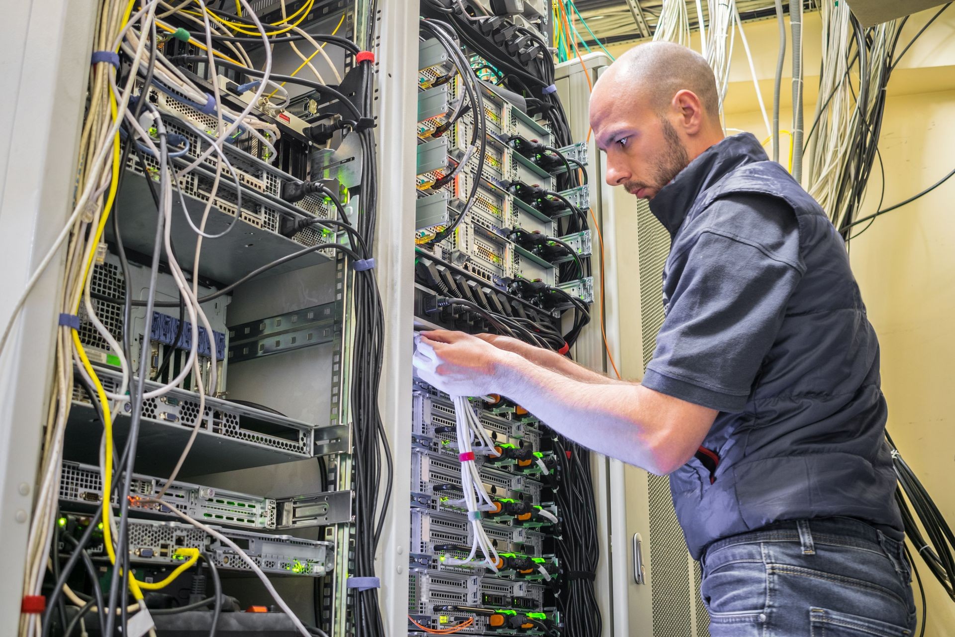A specialist connects the wires in the server room of the data center. A man works with telecommunications equipment. The technician switches the Internet cable of the powerful routers.