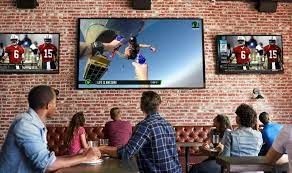 People in a bar watching sports on multiple flat-screen TVs mounted on a brick wall.